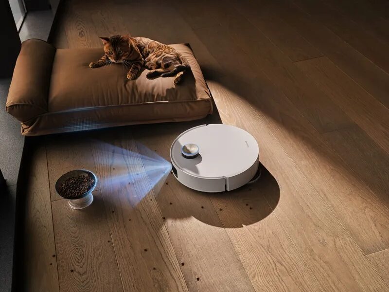 Кот лежит на кровати рядом с роботом Dreame L60 Pro Ultra