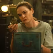 Женщина в серой футболке держит медаль и книгу сериал Silo