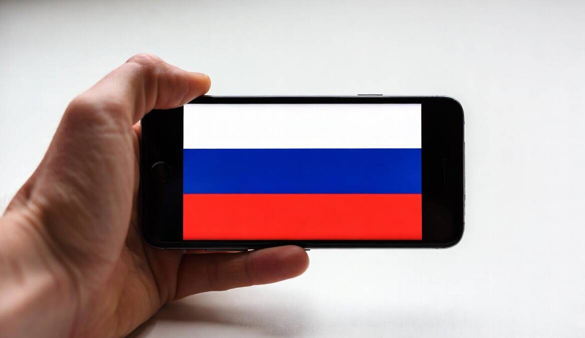 Людская рука держит смартфон с флагом России
