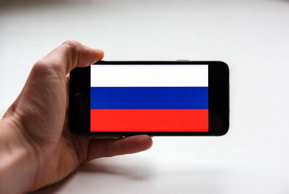 Людская рука держит смартфон с флагом России
