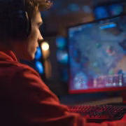 молодой человек с наушниками за компьютером играющий в игру на мониторe Steam