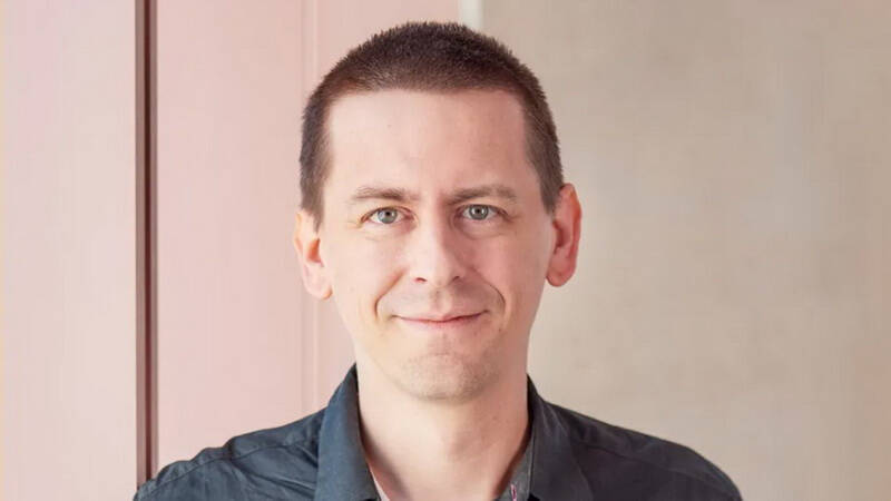 Портрет Джона Джампера, исследователя AlphaFold с короткой стрижкой и синей рубашкой