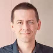 Портрет Джона Джампера, исследователя AlphaFold с короткой стрижкой и синей рубашкой