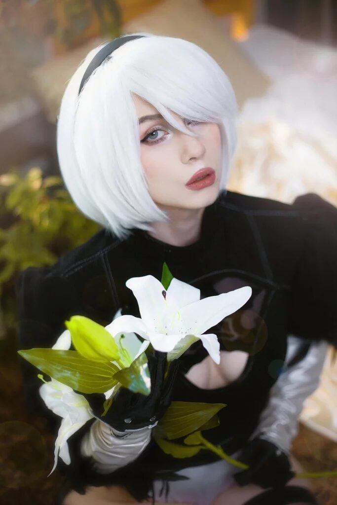 Кос player Nelapochka с белым коротким прической в костюме NieR Automated 2B держит белую лилию крупный план