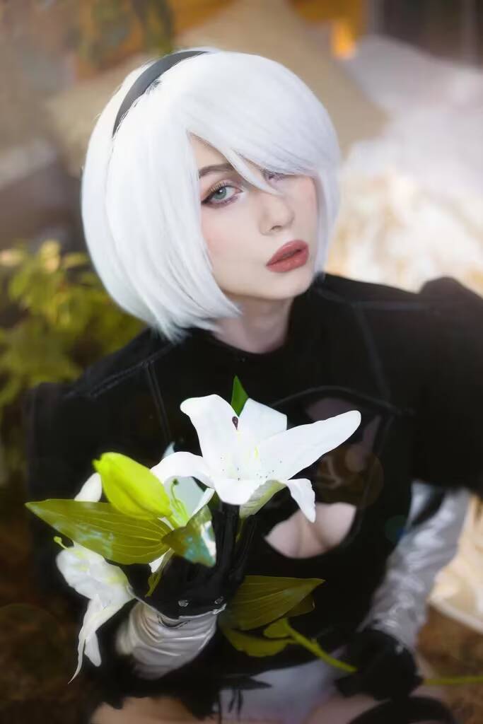 Кос player Nelapochka с белым коротким прической в костюме NieR Automated 2B держит белую лилию крупный план