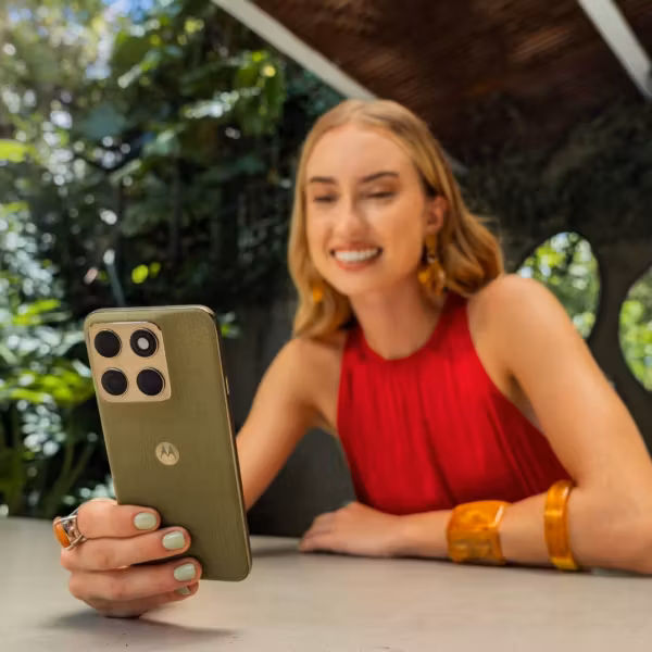 Женщина в красном платье держит телефон Motorola Edge 2026 на открытом воздухе