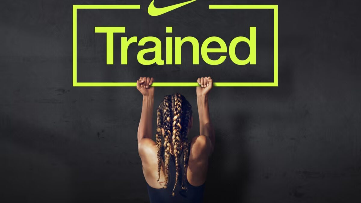 Тренирующаяся женщина держит рамку с надписью Trained на фоне черной стены