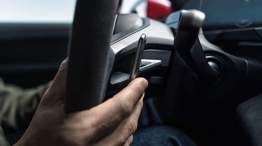 Человек держит смартфон в руке внутри электромобиля Porsche Taycan