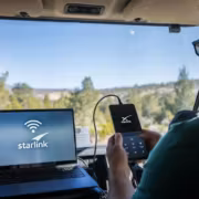 Мужчина использует смартфон и ноутбук с логотипом Starlink в автомобиле зимний пейзаж на заднем плане