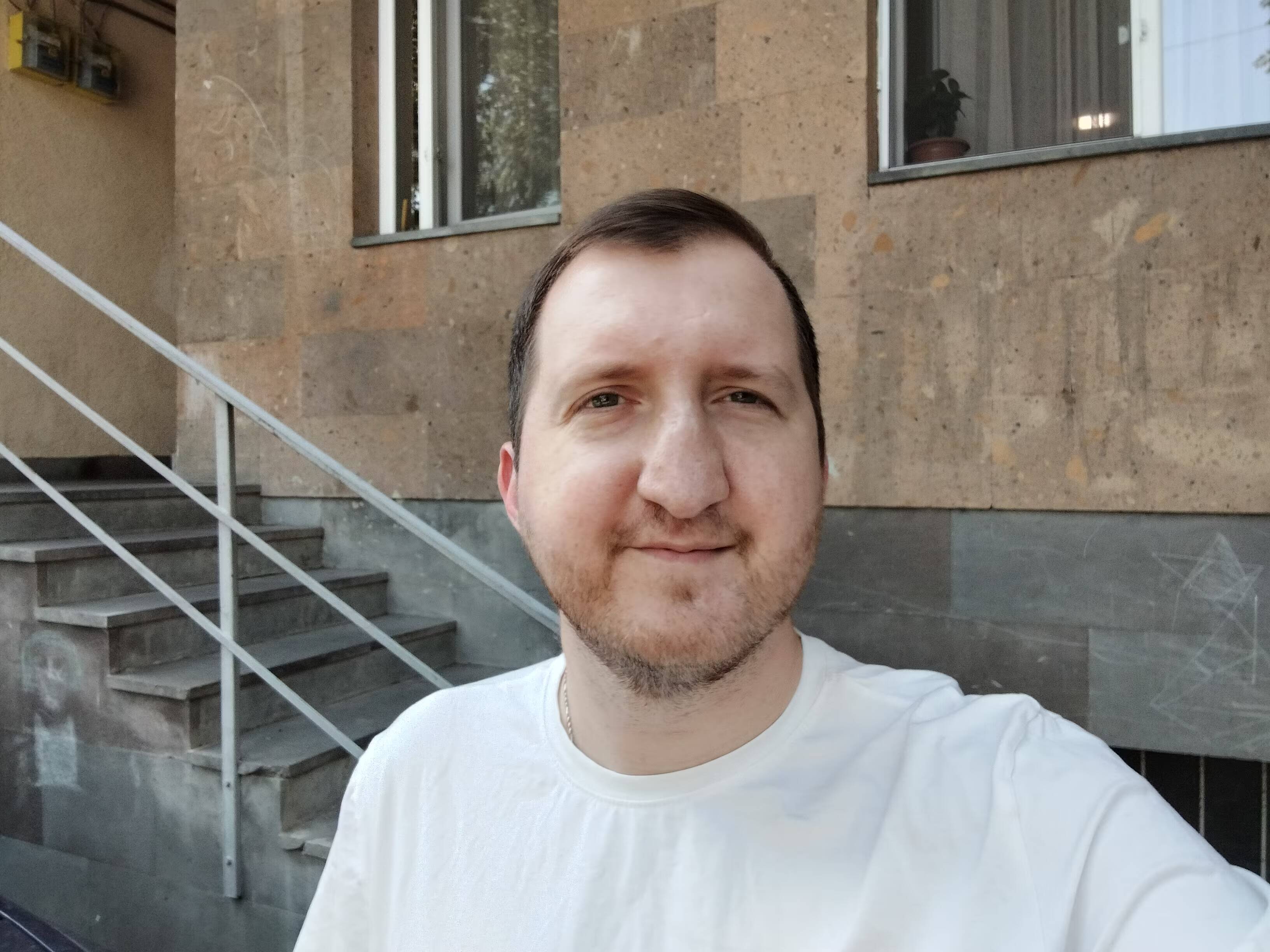 Мужчина в белой футболке на улице возле здания