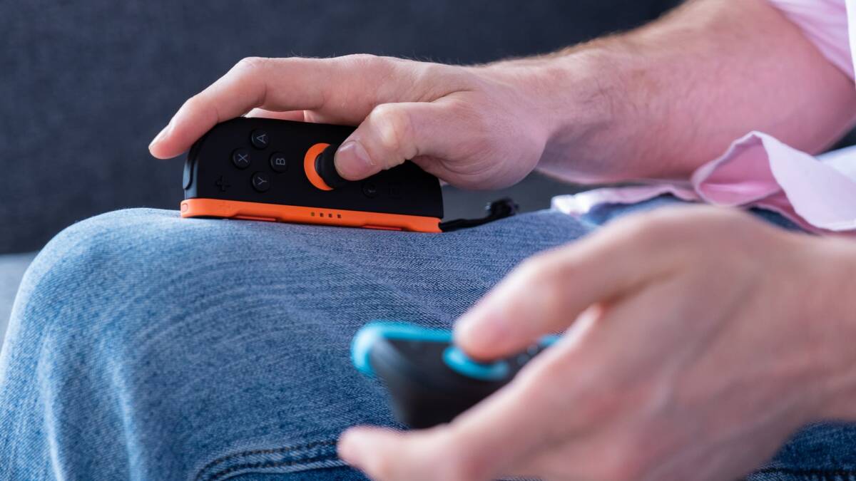 Рука держит игровую консоль Nintendo Switch с черно-оранжевым дизайном