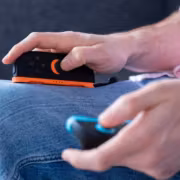 Nintendo отказалась возвращать деньги за подорожавшие консоли из-за тарифов 8 Рука держит игровую консоль Nintendo Switch с черно-оранжевым дизайном