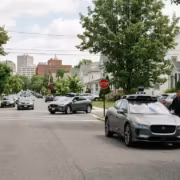 Два человека рядом с серой Tesla Model, улица с машинами и деревьями