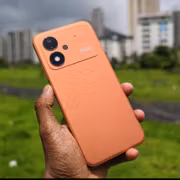 оранжевый смартфон Poco M8 Power на фоне городской среды