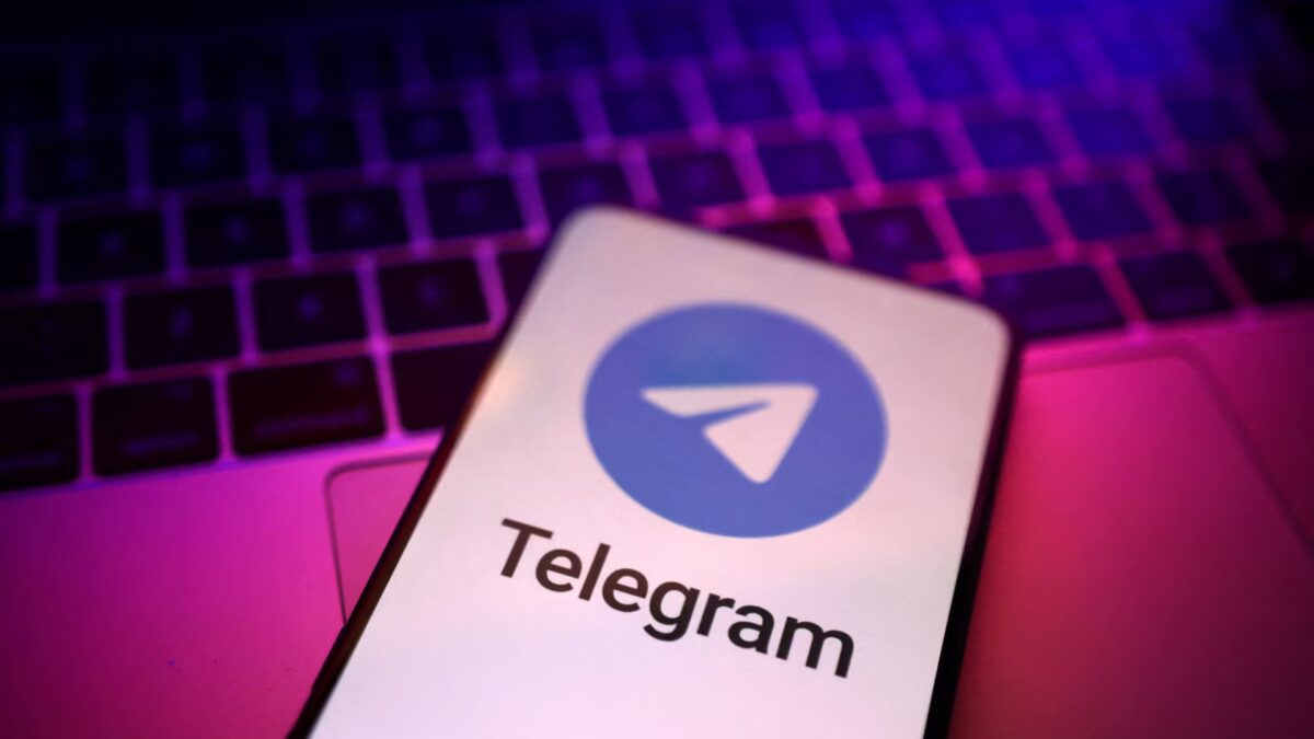 Телеграм на смартфоне с логотипом перед клавиатурой ноутбука