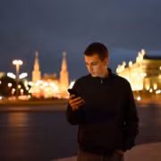 молодой человек в темной куртке смотрит в телефон