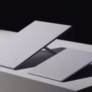 Два MacBook на белом столе, один черный другой белый, поднимающиеся крышки