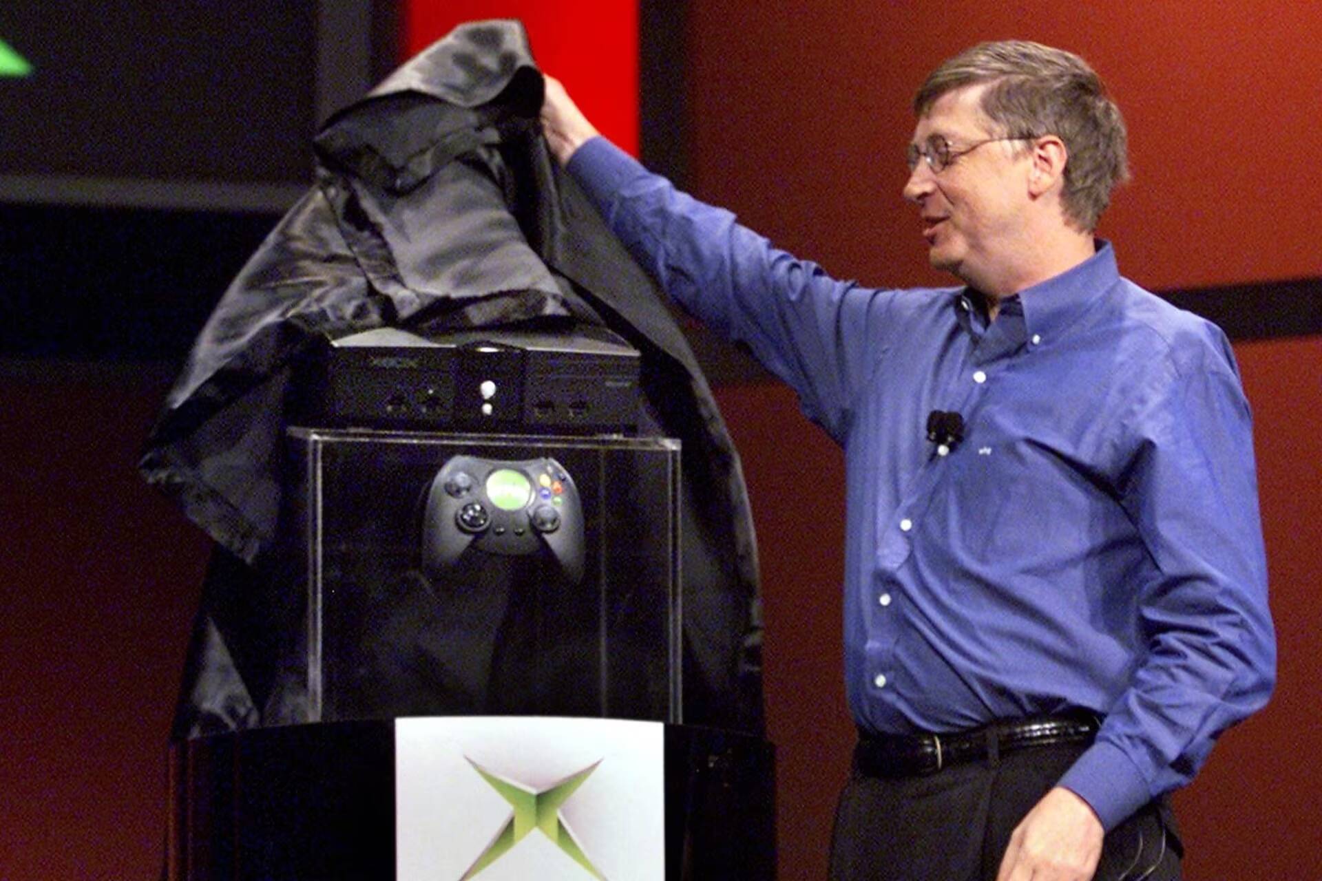Мужчина в голубой рубашке улыбается и трогает облако с Xbox оригинальной консоли