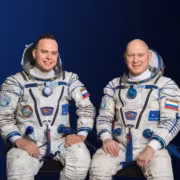 Двое космонавтов в скафандрах Олег Артемьев и Сергей Корсаков на фоне синего цвета во время фотосессии
