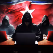 Группа хакеров в тёмных капюшонах у ноутбуков на фоне флага Северной Кореи