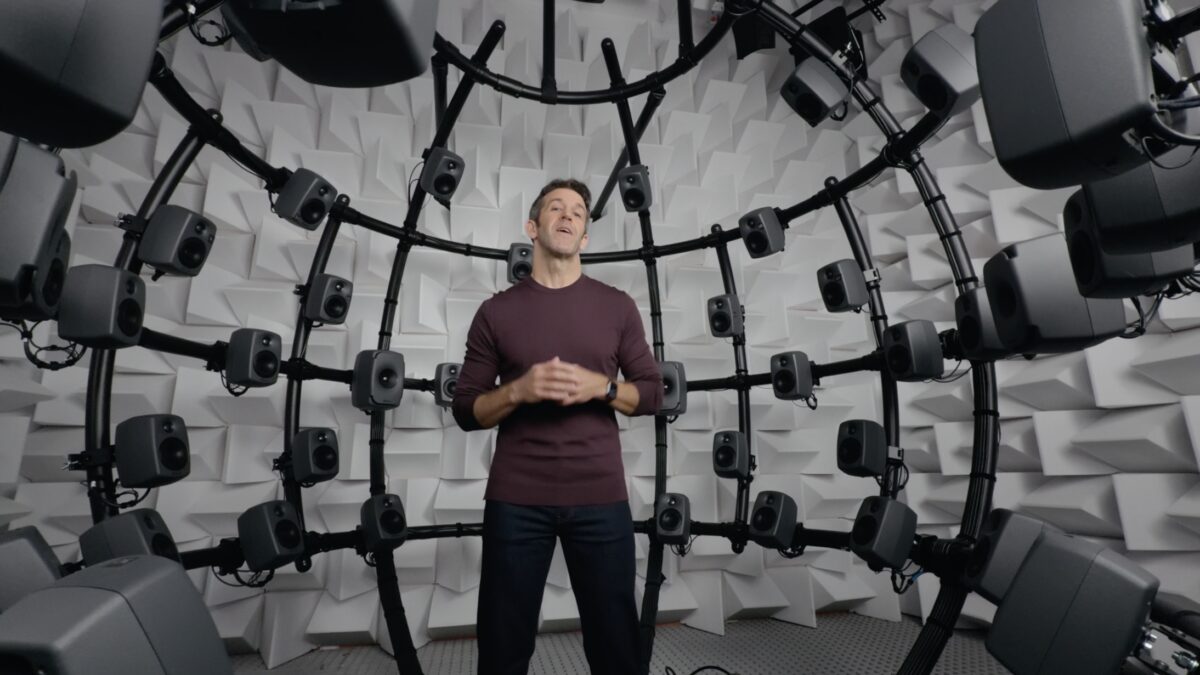 Мужчина в черной кофте у стенда с множеством динамиков AirPods 5 с шумоподавлением