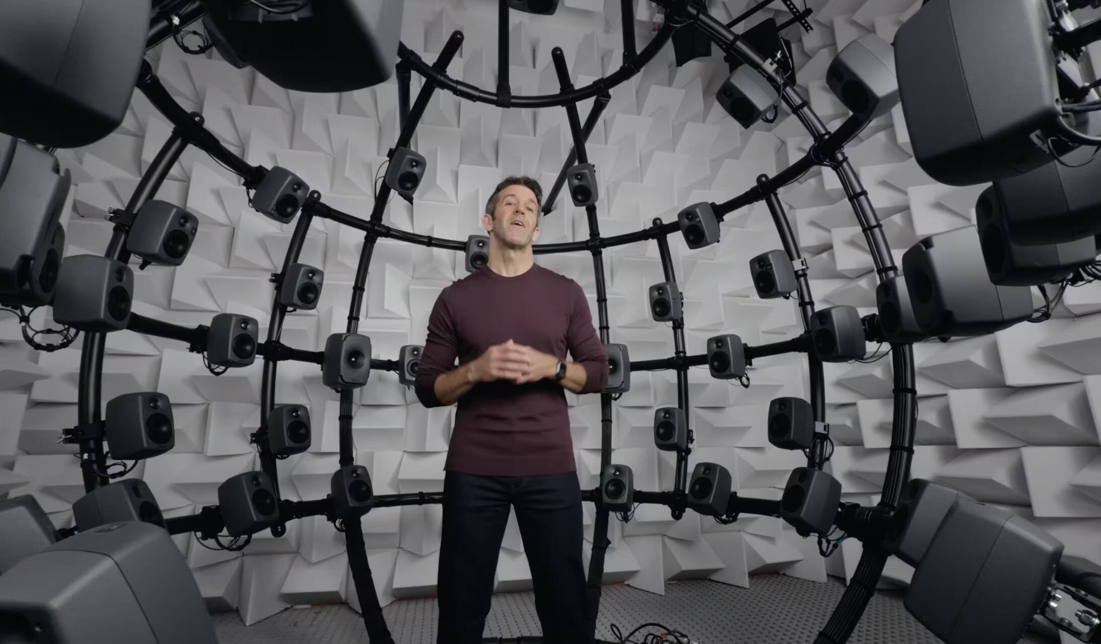 Мужчина в черной кофте у стенда с множеством динамиков AirPods 5 с шумоподавлением