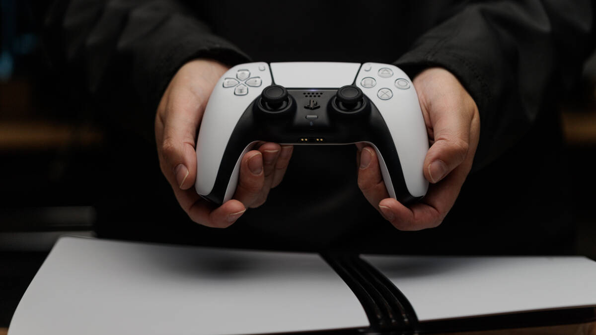 Человек держит белый контроллер PlayStation 5 с двумя антеннами
