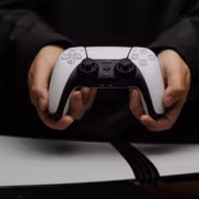 Sony не сокращает выпуск дисков в 2028 году на 90% 2 Человек держит белый контроллер PlayStation 5 с двумя антеннами