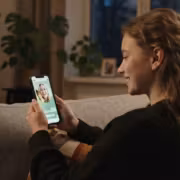 Женщина на диване фотографирует видео Telegram на смартфоне