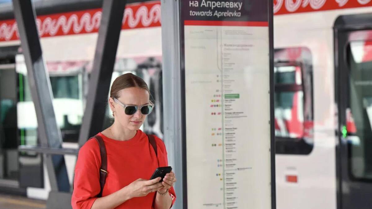 Женщина в красной рубашке использует телефон возле станции метро Билайн 5G