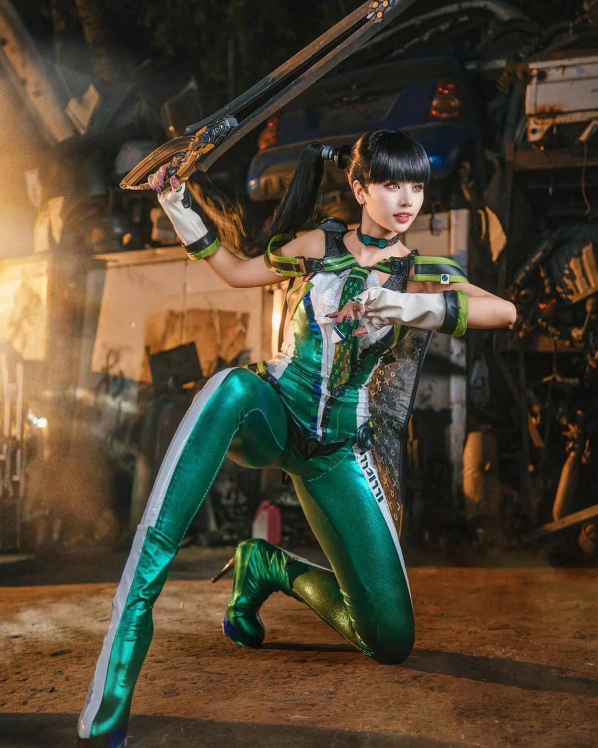 Косплей Евы из Stellar Blade. Charess. Девушка в зеленом костюме держит меч пластиковую ракету с черной ручкой и коричневым лезвием, позирует на фоне гаража с машинами