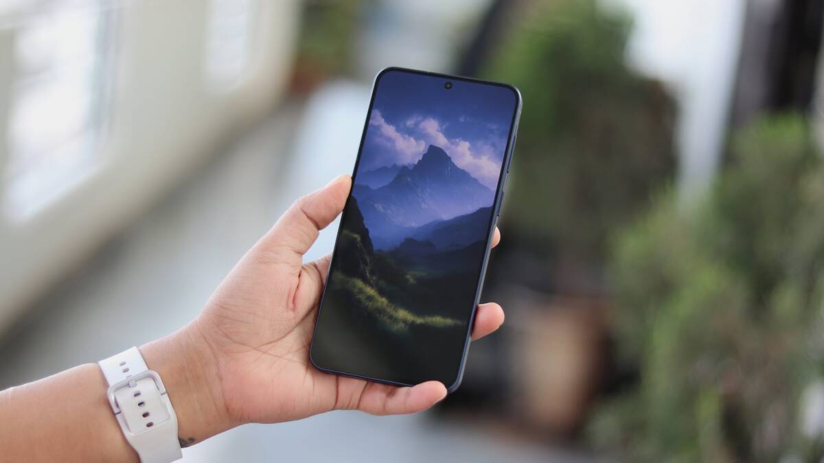 Человек держит смартфон Samsung Galaxy A57 с горным пейзажем на экране