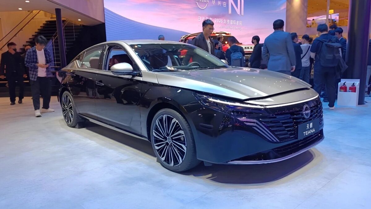 Черный седан Nissan Teana на выставке с людьми вокруг
