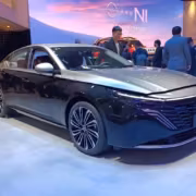 Черный седан Nissan Teana на выставке с людьми вокруг