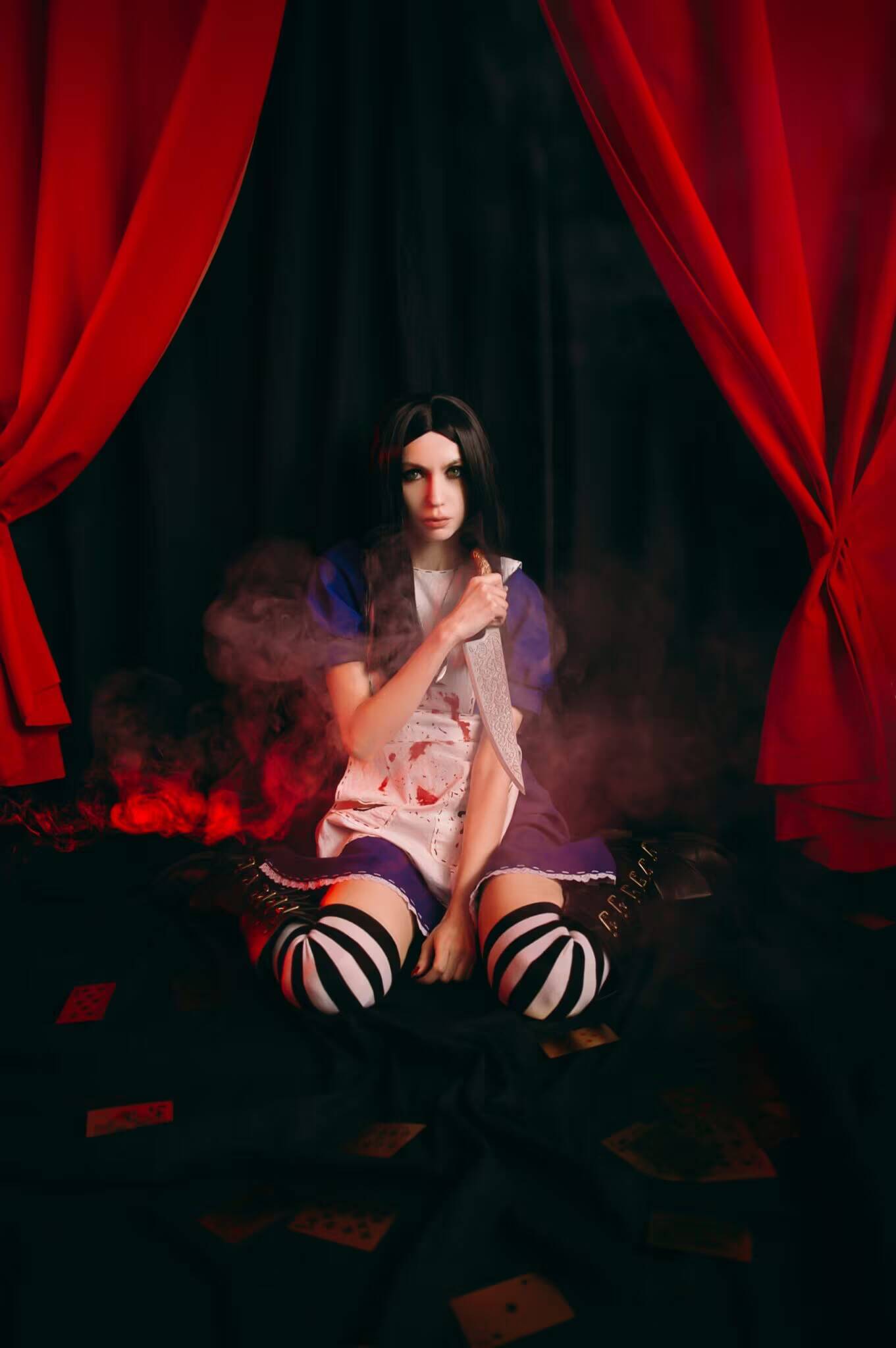 Косплей Алисы Лидделл из Alice Madness Returns. Poison. Девушка с черными волосами и макияжем в стиле готика. На фоне черные шторы и красные занавески