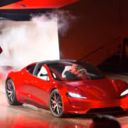 Красная Tesla Roadster на сцене со сцеплением и человеком в кэжуале