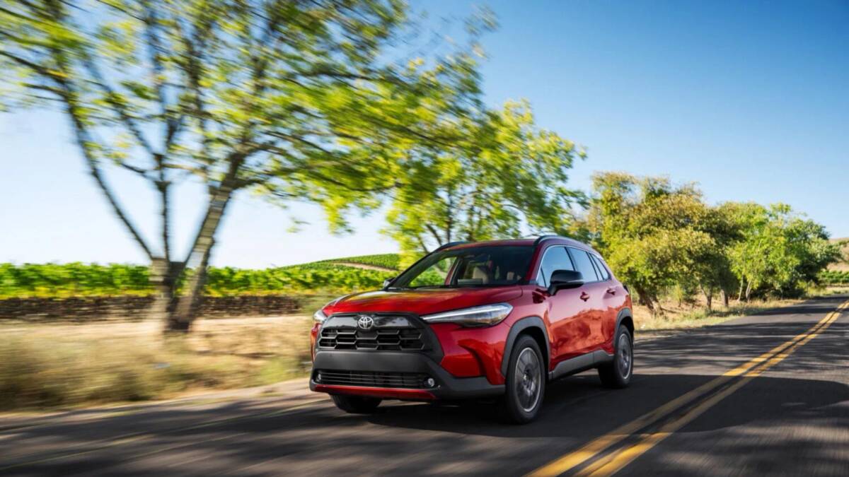 Toyota Corolla Cross 2027 лишилась базового гибрида 3 красный Toyota Corolla Cross едет по дорожке в деревьях