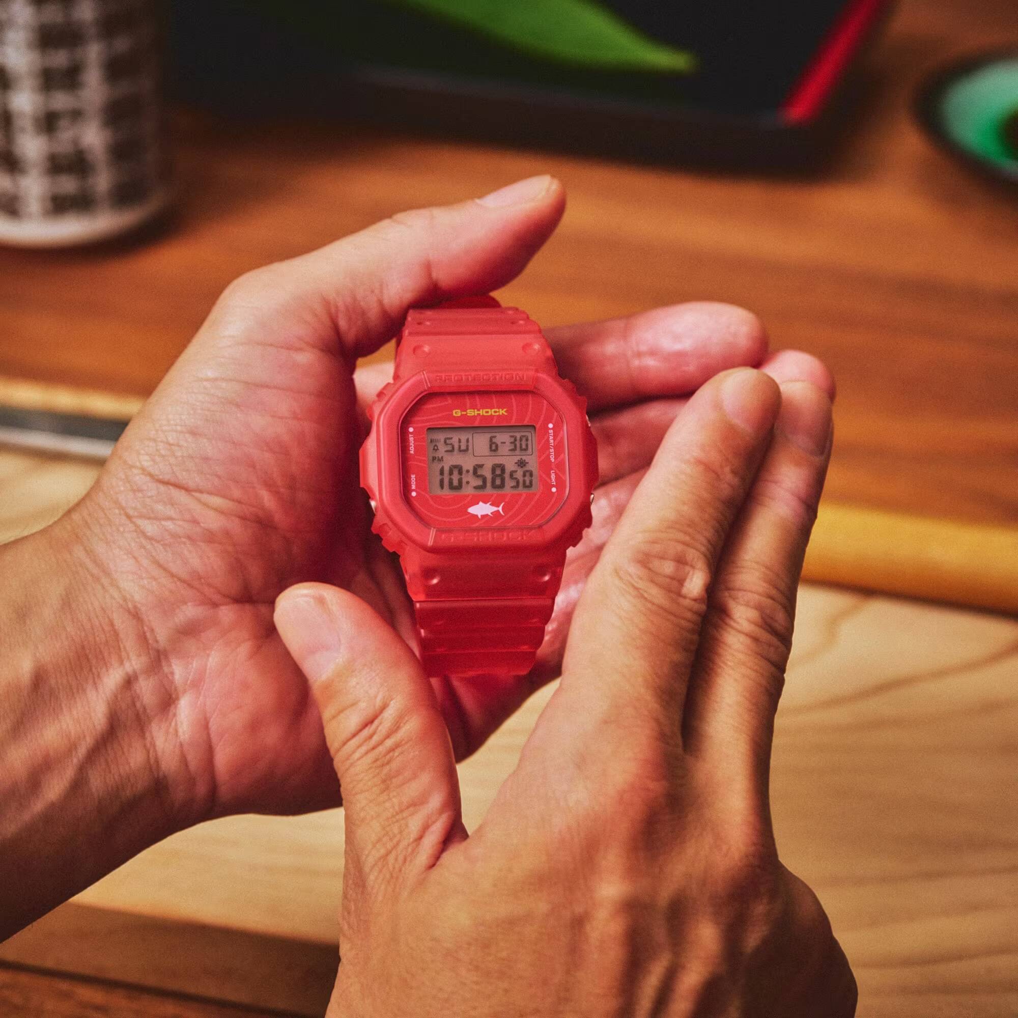 Рука держит красные часы G-Shock с дисплеем
